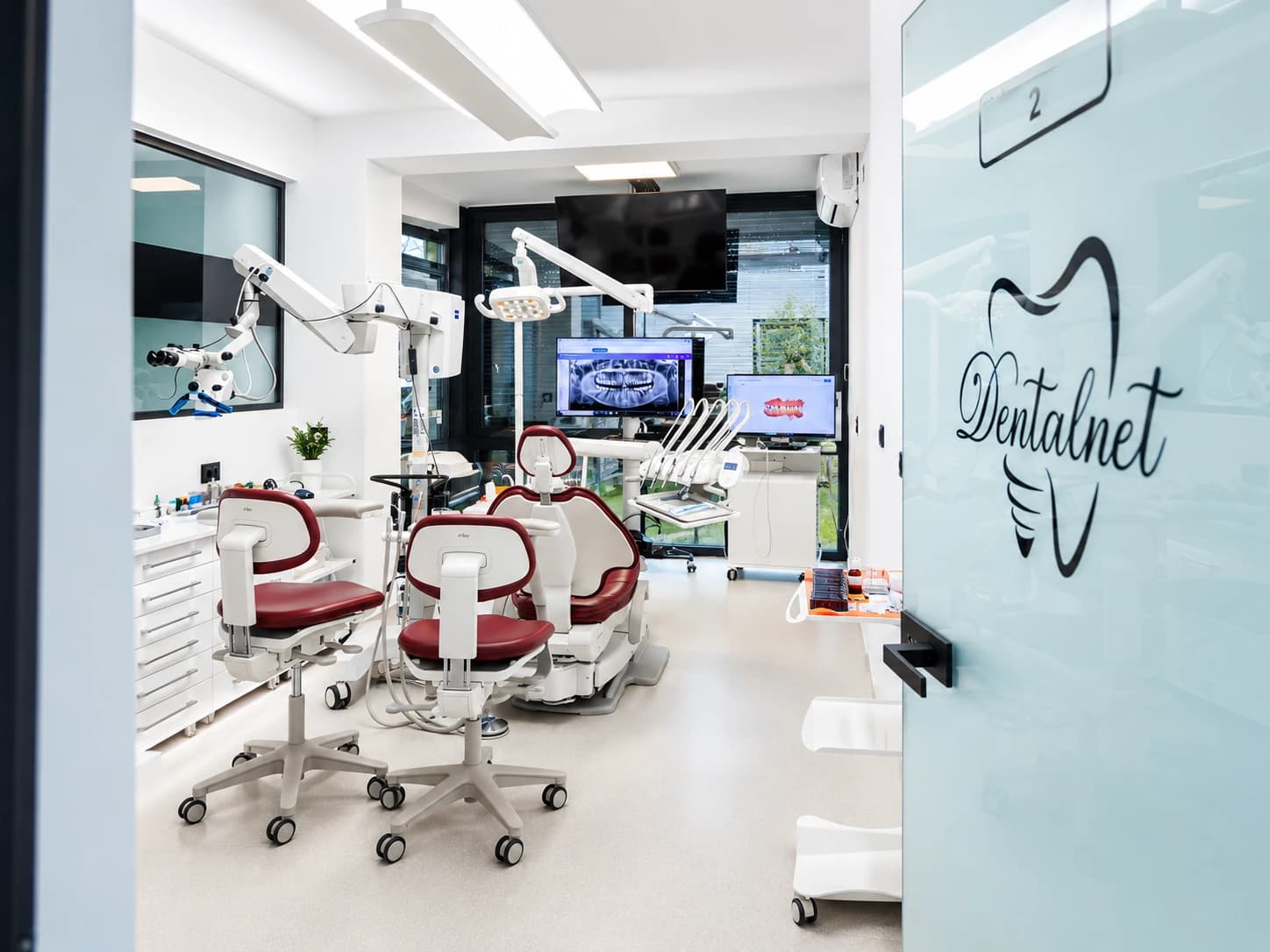 DentalNet treatment room with red chairs and X-ray screens, clinic logo on the door